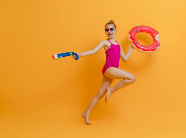 Happy child wearing swimsuit. Girl with swimming ring donut. Kid on a colored yellow background. - Valokuva, kuva