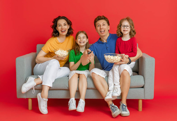Happy loving family on bright colour background. Father, mother and daughters girls watching TV, movies with popcorn. Dad, mom and lovely children are having fun staying at home. - Foto, Bild