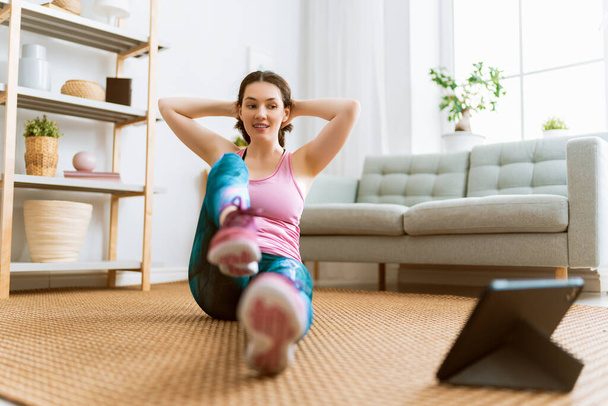 Young woman in activewear watching online courses on tablet while exercising at home. - Fotografie, Obrázek