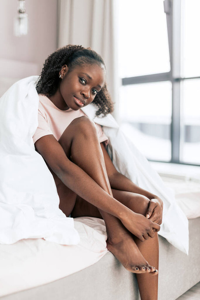 positive girl sitting with raised legs in the bed and looking at the camera - Fotó, kép