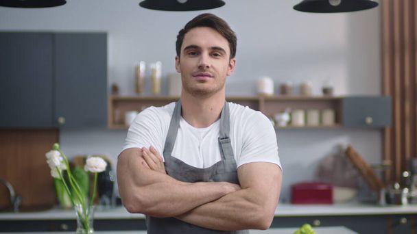Usmívající se kuchař se dívá na kameru v kuchyni. Pohledný muž držící ruce. - Fotografie, Obrázek