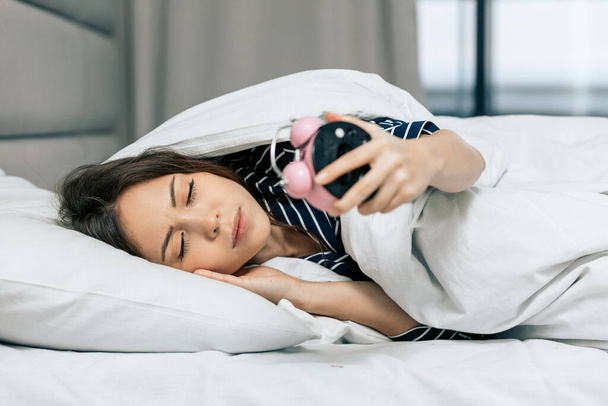 Young sleeping woman looking at alarm clock in bedroom - Fotoğraf, Görsel