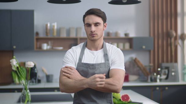 Vážný šéfkuchař hledající kameru v kuchyni. Muž zkříží ruce uvnitř. - Fotografie, Obrázek