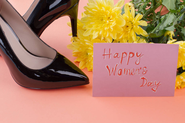 Carte de voeux avec souhaits heureux de la journée des femmes avec des fleurs et des chaussures à talons hauts. - Photo, image