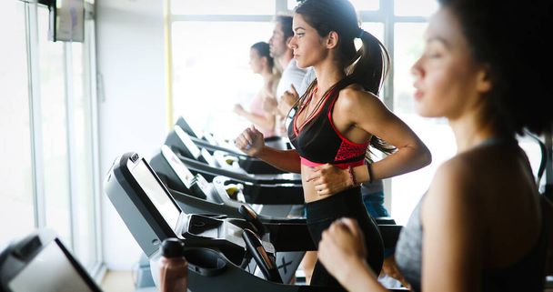 Group of young fit people running on treadmill in gym - Photo, image
