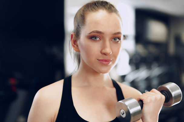 Young brunette sporty woman exercising with dumbbell in a gym - Fotoğraf, Görsel