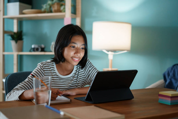Homeschooling Asian girl doing homework And study online with tutor on tablet at desk at night. - Foto, Imagem