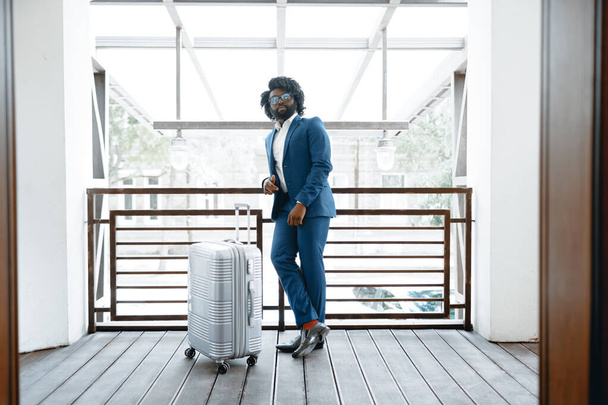 Hombre negro en traje formal con maleta empacada entrando en la puerta del hotel - Foto, imagen