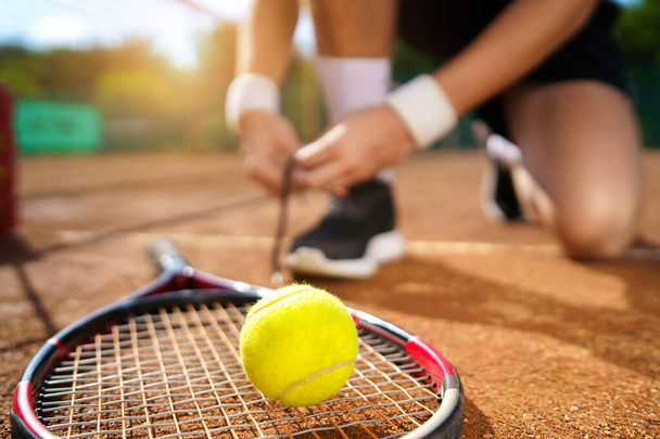 Tennispelaaja sitomassa kengännauhojaan. Valikoiva painopiste pallo ja maila - Valokuva, kuva