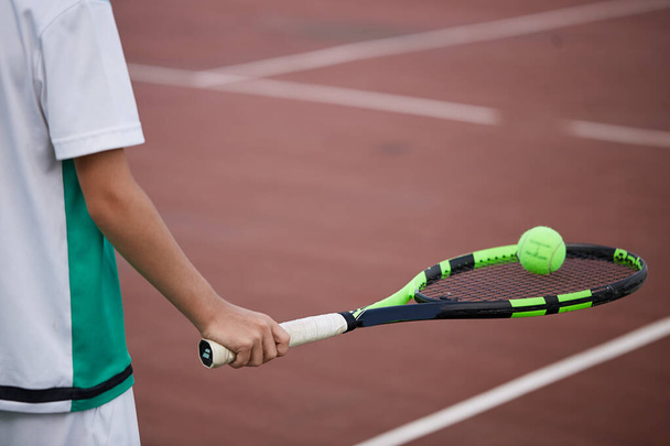 Close-up of male hand holding tennis ball and racket on red-clay court. - Fotó, kép