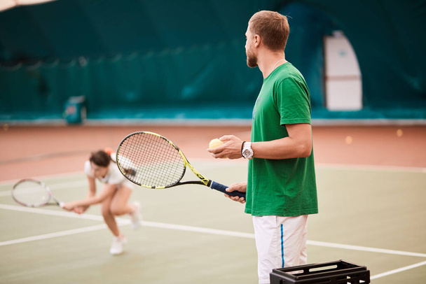 Young bearded man in green sportwear is playing tennis on indoor court. - Zdjęcie, obraz