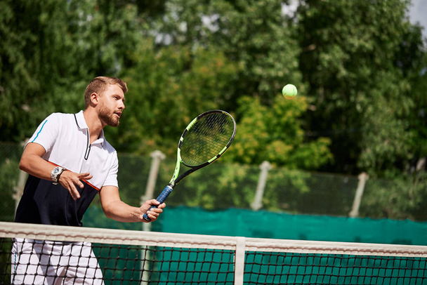 Jeune homme en vêtements de sport joue au tennis sur le court de porte. - Photo, image