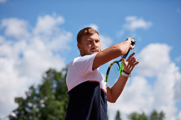 Young man in sportwear is playing tennis on out door court. - Foto, afbeelding