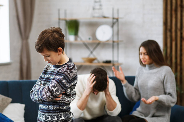Sad little boy feels upset while his parents fighting at background. Mother and father quarrel. Family conflicts and divorce lead to childrens psychological problem. Childrens mental disorders - Foto, Imagen