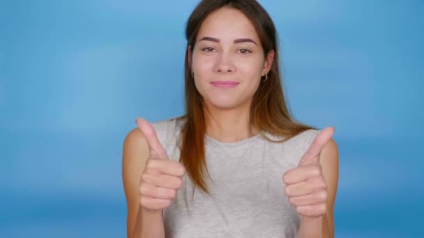 Pozitív nő szürke pólóban mutogatja a hüvelykujját, táncol és mosolyog. - Felvétel, videó