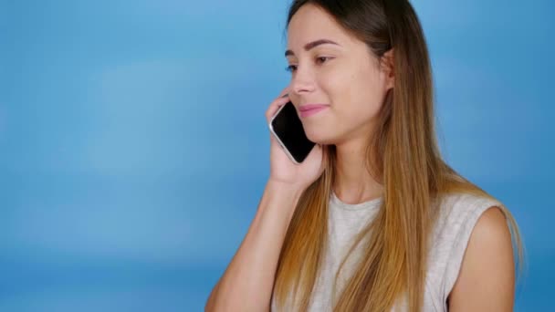 Woman in gray T-shirt takes phone call, brings smartphone to ear and says hello - Filmagem, Vídeo