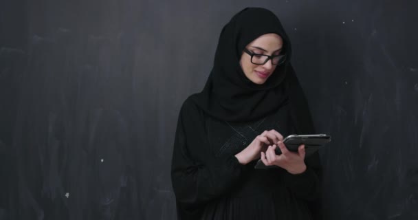 young modern muslim business woman using smartphone wearing hijab clothes in front of black chalkboard - Felvétel, videó