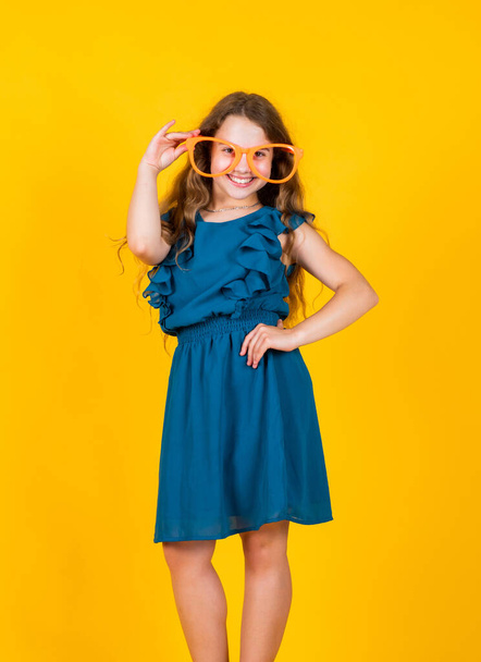party glasses for fun. female hairdresser salon. beauty and summer fashion. cheerful child on yellow background. trendy kid. happy childhood. small girl has long lush hair. kid in dress - Foto, Bild