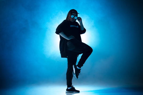 Young hip-hop female dancer performing solo on the stage in blue neon lights - 写真・画像