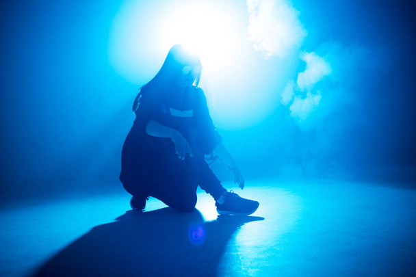 Young hip-hop female dancer performing solo on the stage in blue neon lights - Photo, image
