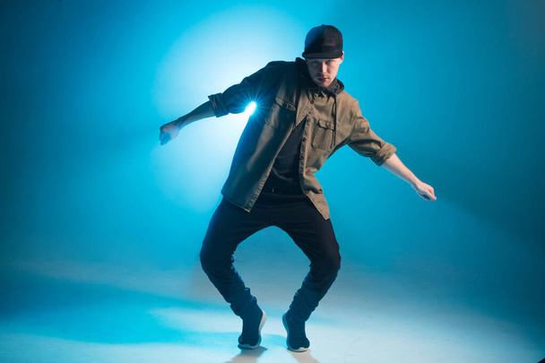 Young man dancer dancing funky hip hop on isolated studio neon blue background - Fotoğraf, Görsel
