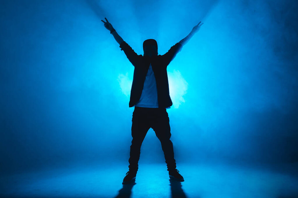 Sporty modern style hip-hop dancer shows his dance on blue studio background. - Fotoğraf, Görsel