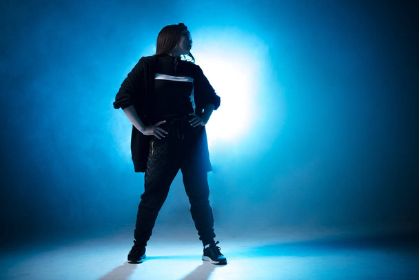 Young woman hip-hop dancer on studio blue light background with flare effects - Fotó, kép