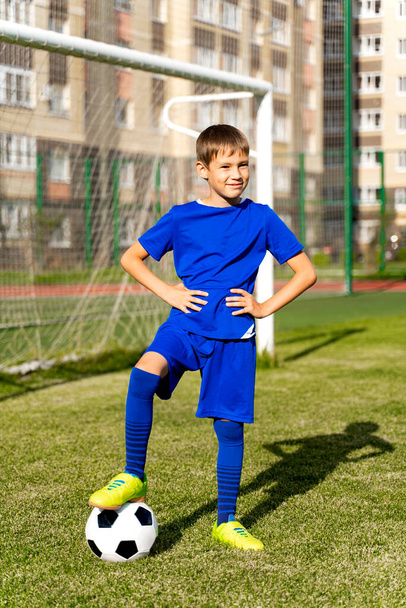 Маленький футболист с мячом стоит на зеленом футбольном поле в воротах. - Фото, изображение