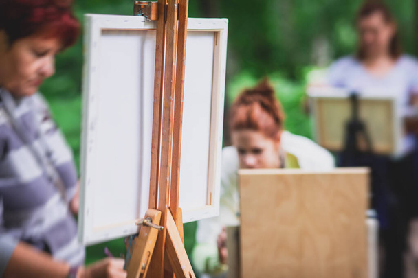Process of plein air painting, group class of adult talented students in the park with paints easels, and canvases during lesson of watercolour painting outdoors  - Fotografie, Obrázek