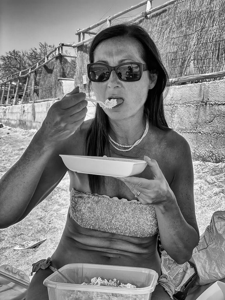 Μια γυναίκα στην παραλία τρώει φαστφουντάδικο. Χρόνος διακοπών. - Φωτογραφία, εικόνα