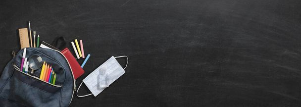 School bag mask, disinfectant and school supplies on chalkboard. Coronavirus measures and back to school concept - Φωτογραφία, εικόνα