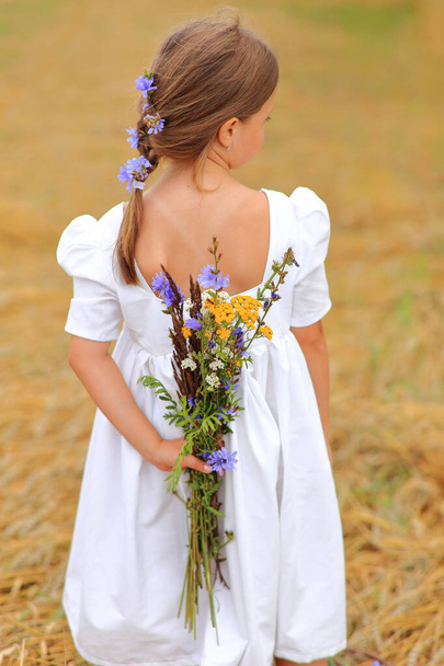 Dívka s kyticí divokých květin v rukou na pšeničném poli. - Fotografie, Obrázek