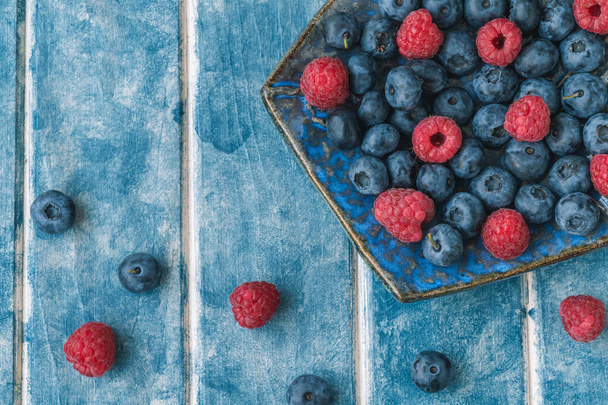 食べ物の背景。ブルーベリーのエスノプレート、青い背景のラズベリー. - 写真・画像