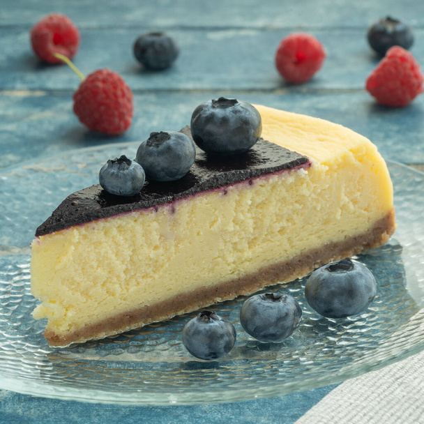 Blueberry and raspberry cheesecake, served on a transparent plate with brown sugar. Glass of milk on a light blue wooden background. - Photo, Image