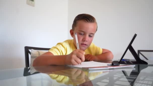 Мальчик делает домашнее задание дома на обеденном столе, концентрируется и думает, пока в школе перерыв.. - Кадры, видео