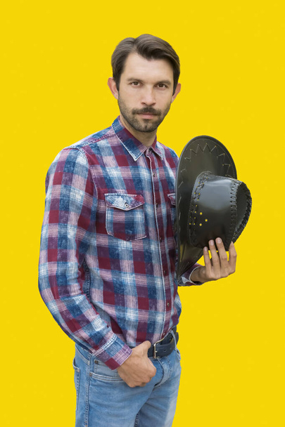 a young cowboy on a yellow background holds his hat in his hand - Φωτογραφία, εικόνα