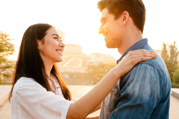 Image of romantic multicultural couple smiling and looking at each other while hugging outdoors - Photo, image