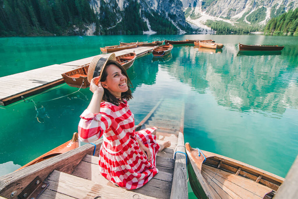 donna in sundress rosso seduta su scale di legno guardando il lago in montagna - Foto, immagini