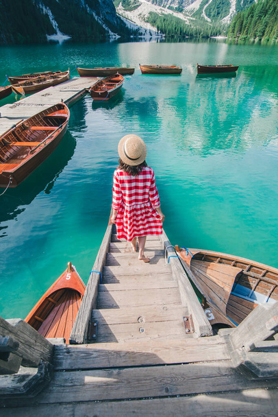 νεαρή ευγενική γυναίκα σε κόκκινο καρό φόρεμα ξυπόλητη με τα πόδια από ξύλινες σκάλες του σταθμού βάρκα οδηγεί στη λίμνη - Φωτογραφία, εικόνα