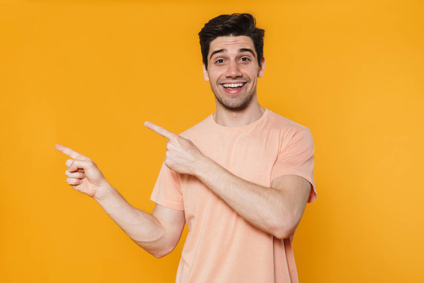 Photo of joyful handsome man smiling and pointing fingers aside isolated over yellow background - Fotografie, Obrázek