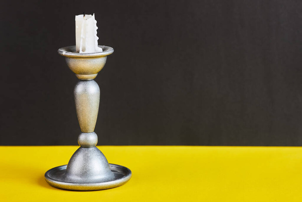 Metal curved white candlestick with thick wjite candle isolated on black and yellow background. - Zdjęcie, obraz