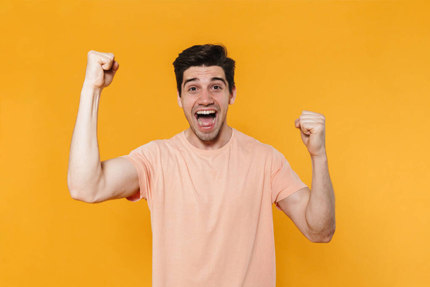 Photo of delighted handsome man screaming and making winner gesture isolated over yellow background - Fotó, kép