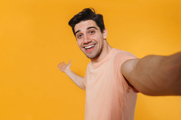 Photo of happy handsome man smiling and taking selfie photo isolated over yellow background - Фото, изображение