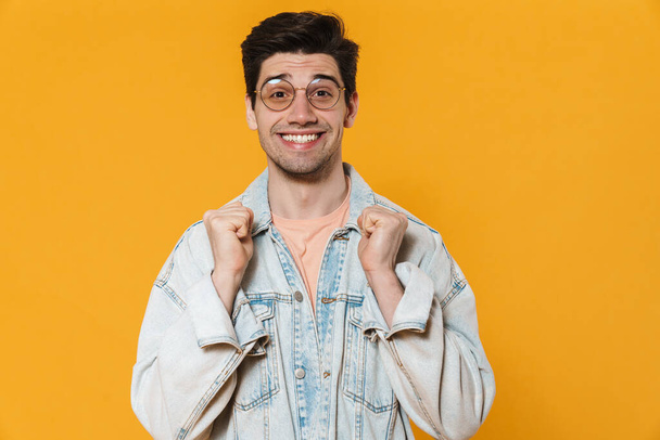 Photo of joyful young man in eyeglasses smiling and looking at camera isolated over yellow background - Foto, Imagem