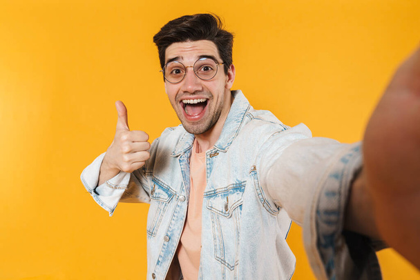 Photo of delighted bristle man showing thumb up while taking selfie photo isolated over yellow background - Foto, afbeelding