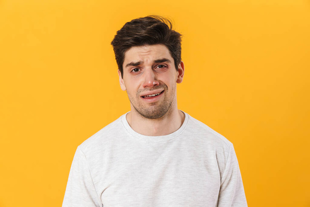 Photo of unhappy bristle man in basic t-shirt posing and looking on camera isolated over yellow background - Фото, зображення