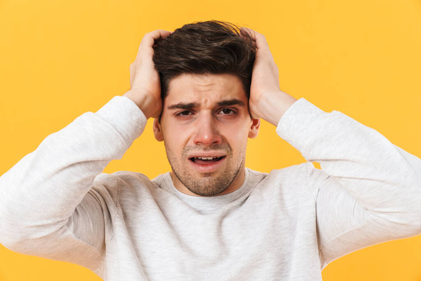 Photo of sick unhappy man having headache and grabbing his head isolated over yellow background - Foto, Imagem
