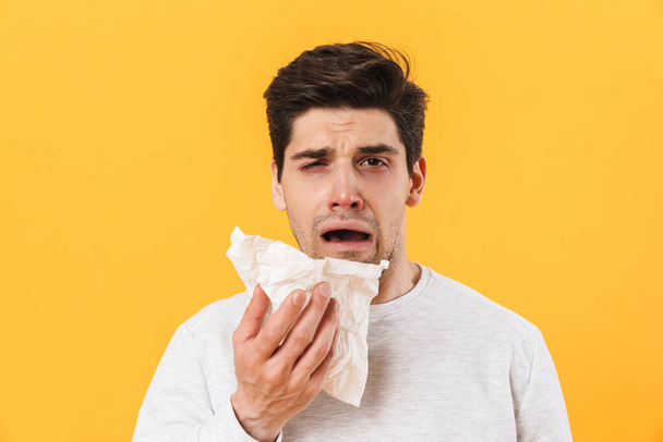 Photo of sick unhappy man with runny nose posing with tissue on camera isolated over yellow background - Fotoğraf, Görsel