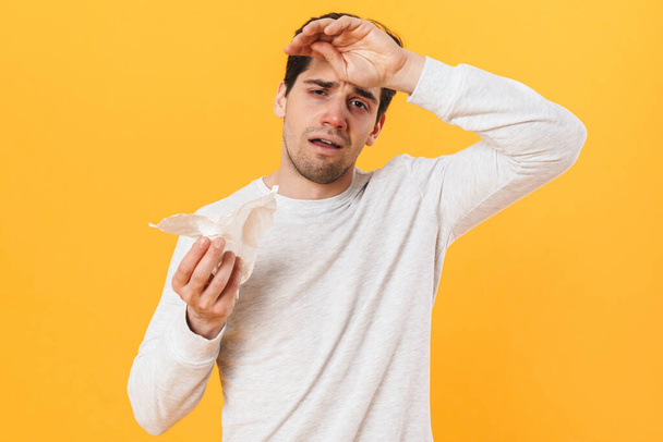 Photo of sick unhappy man with runny nose posing with tissue on camera isolated over yellow background - Φωτογραφία, εικόνα