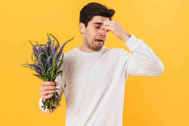 Photo of handsome unhappy man with allergy posing with flowers isolated over yellow background - Foto, Imagen
